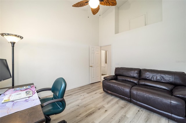 office area with light wood-type flooring, a ceiling fan, a high ceiling, and baseboards