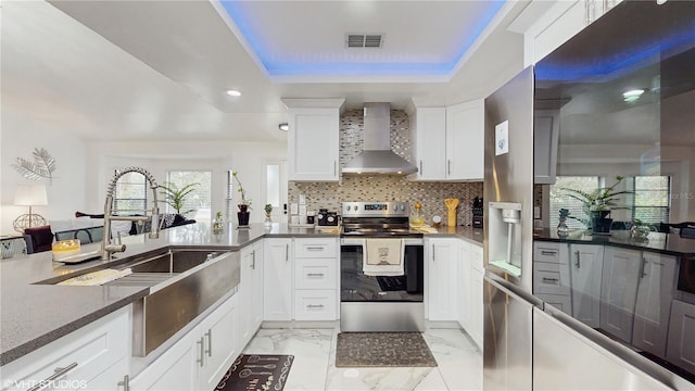 kitchen with wall chimney exhaust hood, a tray ceiling, electric stove, decorative backsplash, and white cabinets