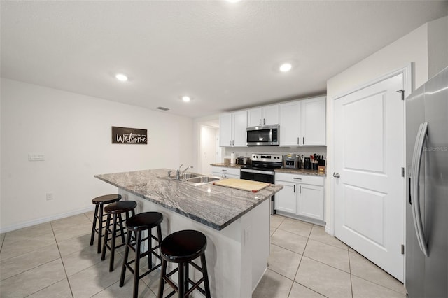 kitchen with stone counters, white cabinetry, an island with sink, and appliances with stainless steel finishes