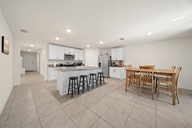 kitchen featuring a breakfast bar, a center island with sink, white cabinets, light tile patterned floors, and stainless steel appliances