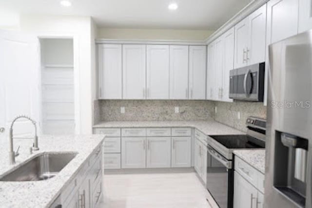 kitchen with light stone countertops, backsplash, stainless steel appliances, sink, and white cabinetry