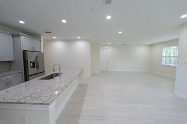 kitchen featuring light stone countertops, stainless steel refrigerator with ice dispenser, and gray cabinets