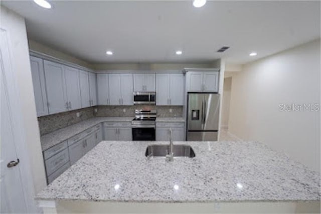 kitchen with light stone countertops, appliances with stainless steel finishes, decorative backsplash, sink, and a kitchen island