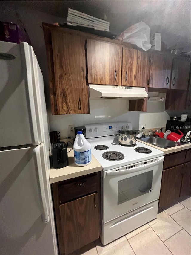 kitchen with sink, white appliances, light tile patterned floors, and dark brown cabinetry