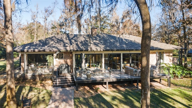 rear view of property featuring a lawn, a wooden deck, and a sunroom