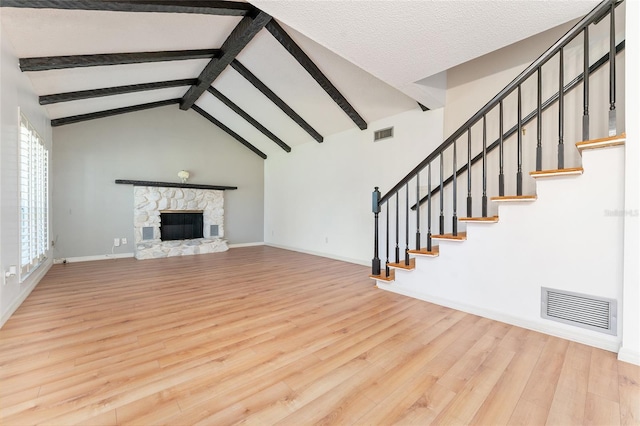 unfurnished living room featuring a stone fireplace, beamed ceiling, high vaulted ceiling, hardwood / wood-style floors, and a textured ceiling