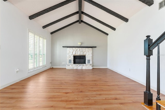 unfurnished living room with a stone fireplace, beamed ceiling, light hardwood / wood-style floors, and high vaulted ceiling