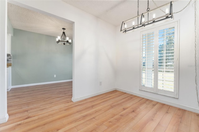 unfurnished dining area with wood-type flooring, a textured ceiling, an inviting chandelier, and plenty of natural light