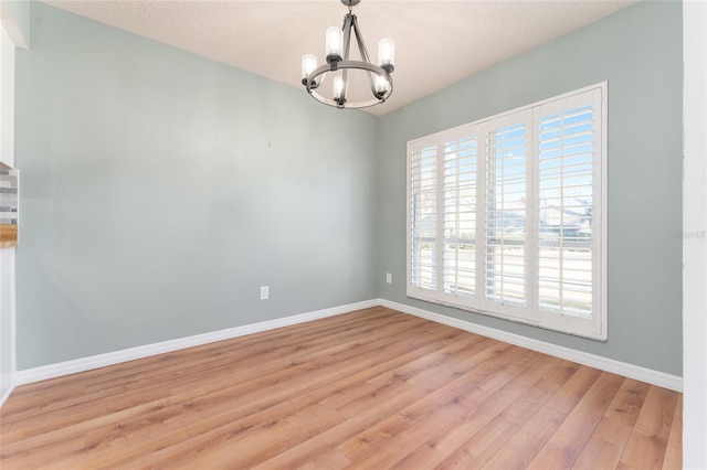 unfurnished room featuring light hardwood / wood-style floors, a textured ceiling, and a notable chandelier