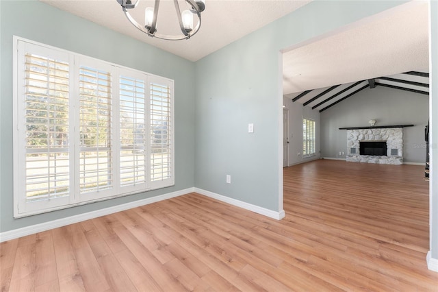 unfurnished living room featuring a fireplace, lofted ceiling with beams, light hardwood / wood-style flooring, and an inviting chandelier