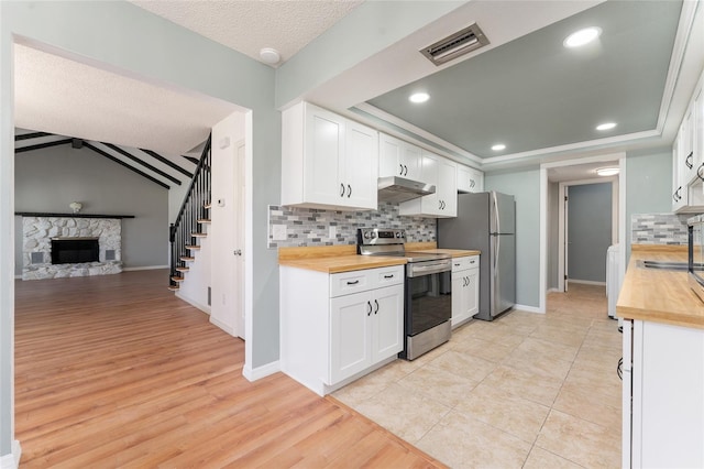 kitchen with wood counters, a stone fireplace, white cabinetry, and stainless steel appliances