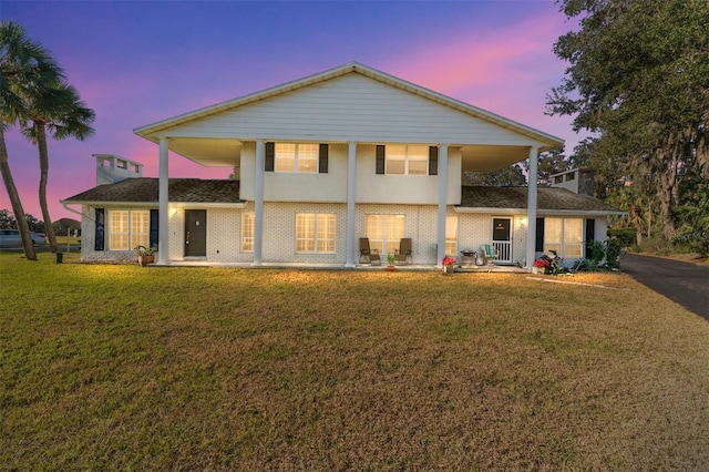 back house at dusk featuring a lawn