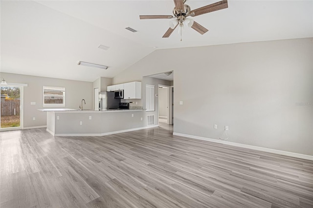 unfurnished living room featuring ceiling fan, vaulted ceiling, sink, and light hardwood / wood-style flooring