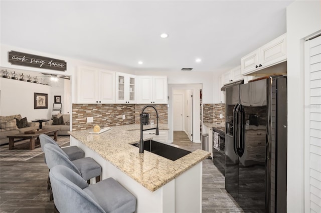 kitchen with black fridge with ice dispenser, sink, white cabinetry, kitchen peninsula, and light stone countertops