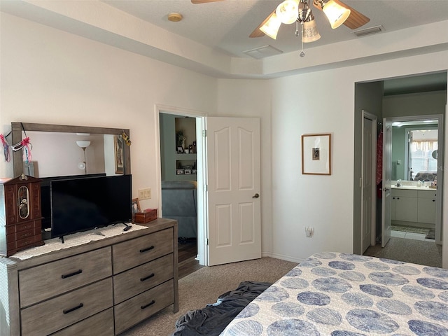 bedroom with light carpet, ensuite bathroom, a raised ceiling, and ceiling fan