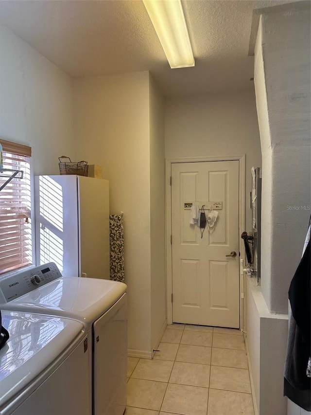 clothes washing area featuring washer and dryer, a textured ceiling, and light tile patterned flooring