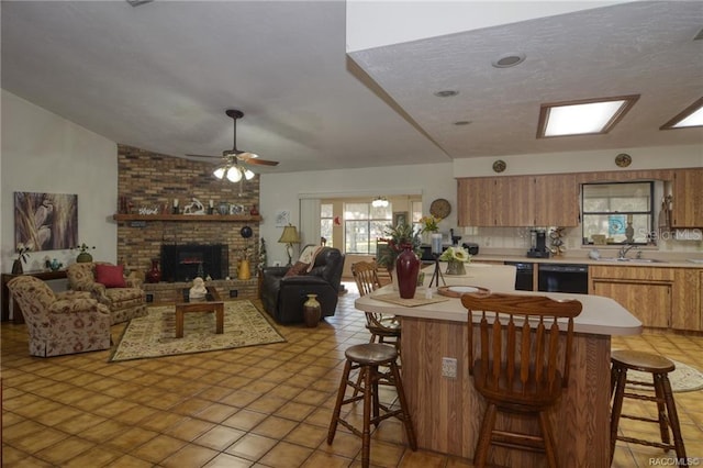 kitchen with a breakfast bar, black dishwasher, a brick fireplace, and ceiling fan