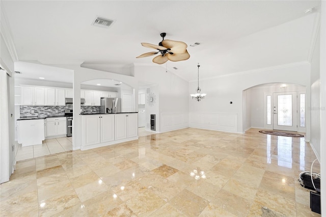 unfurnished living room with vaulted ceiling, ceiling fan with notable chandelier, and ornamental molding