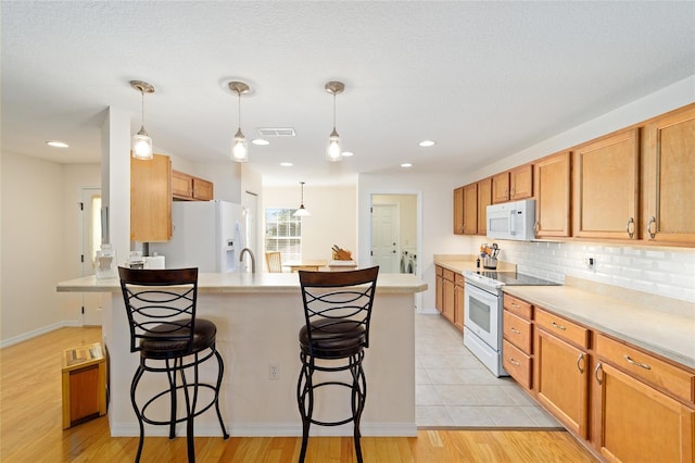 kitchen featuring pendant lighting, a breakfast bar, white appliances, and backsplash