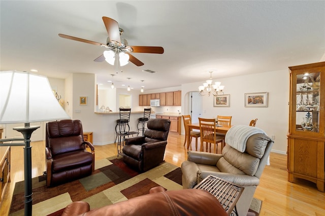 living room with ceiling fan with notable chandelier and light hardwood / wood-style flooring