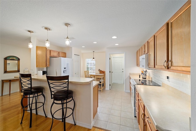 kitchen featuring a kitchen bar, white appliances, backsplash, and hanging light fixtures