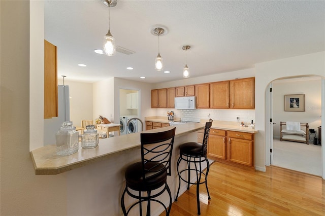 kitchen with hanging light fixtures, a kitchen breakfast bar, separate washer and dryer, kitchen peninsula, and decorative backsplash