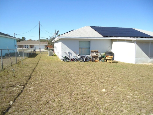 back of property with a yard, central AC unit, and solar panels