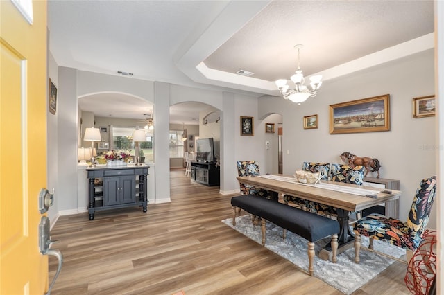 dining area with a tray ceiling, a notable chandelier, and light hardwood / wood-style floors