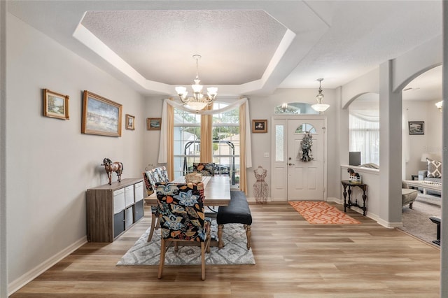 dining space featuring a tray ceiling, a chandelier, a textured ceiling, and light wood-type flooring