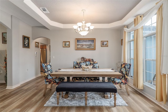 dining space with a textured ceiling, a tray ceiling, an inviting chandelier, and light hardwood / wood-style floors