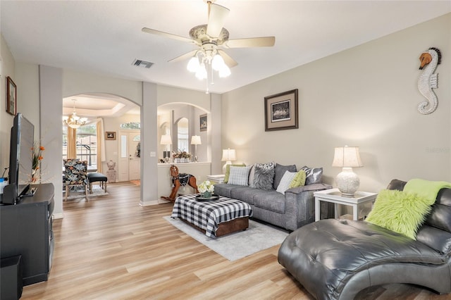 living room featuring ceiling fan with notable chandelier and light wood-type flooring