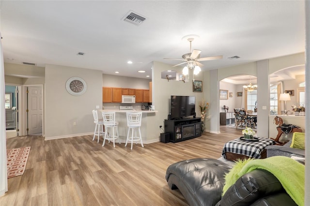 living room featuring ceiling fan with notable chandelier and light hardwood / wood-style flooring