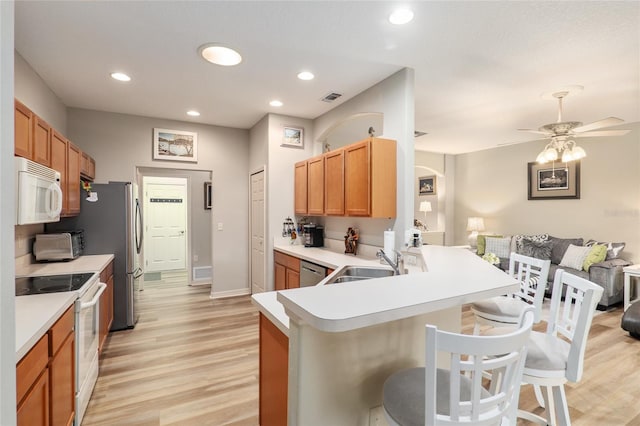 kitchen with kitchen peninsula, a kitchen breakfast bar, stainless steel appliances, sink, and light hardwood / wood-style floors