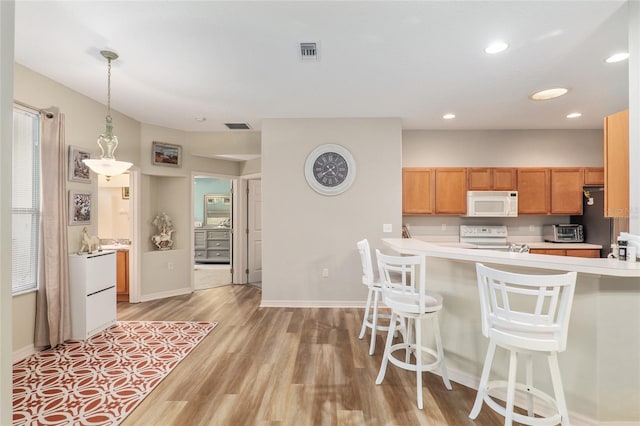 kitchen featuring kitchen peninsula, a kitchen breakfast bar, light wood-type flooring, white appliances, and decorative light fixtures