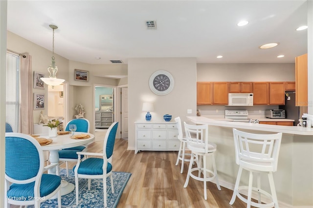 kitchen featuring white appliances, a kitchen breakfast bar, light hardwood / wood-style flooring, decorative light fixtures, and kitchen peninsula