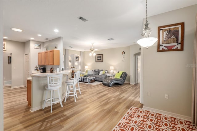 kitchen with kitchen peninsula, a kitchen breakfast bar, ceiling fan, light brown cabinets, and light hardwood / wood-style flooring