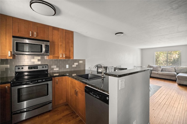 kitchen featuring sink, dark stone countertops, dark hardwood / wood-style flooring, kitchen peninsula, and stainless steel appliances