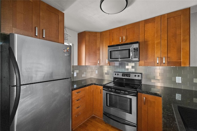 kitchen featuring sink, backsplash, dark stone countertops, appliances with stainless steel finishes, and hardwood / wood-style flooring