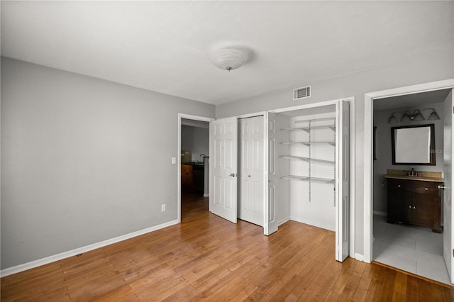 unfurnished bedroom with ensuite bathroom, light wood-type flooring, sink, and multiple closets