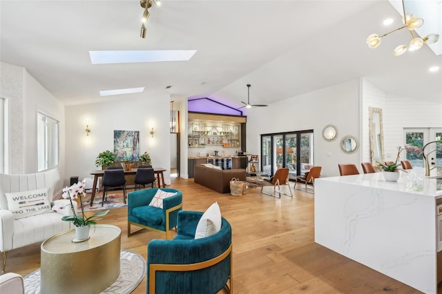 living room featuring vaulted ceiling with skylight, ceiling fan with notable chandelier, and light hardwood / wood-style floors