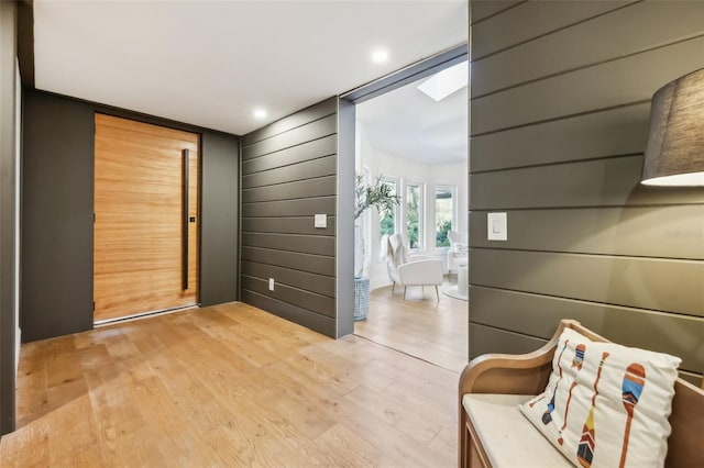 interior space featuring light wood-type flooring, a skylight, and wood walls