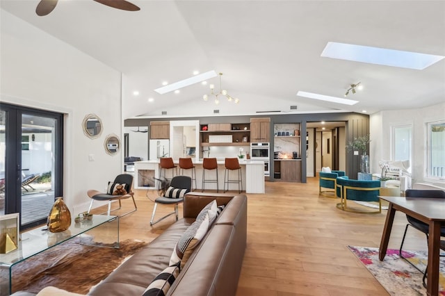 living room featuring vaulted ceiling with skylight, ceiling fan with notable chandelier, and light wood-type flooring