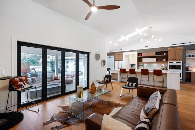 living room with ceiling fan with notable chandelier, light wood-type flooring, and vaulted ceiling