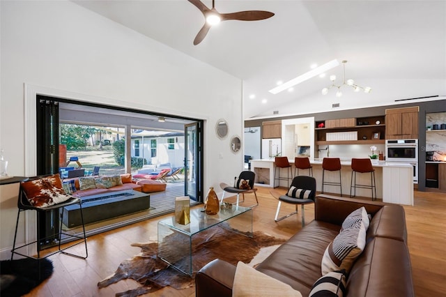 living room with ceiling fan with notable chandelier, light hardwood / wood-style floors, and lofted ceiling