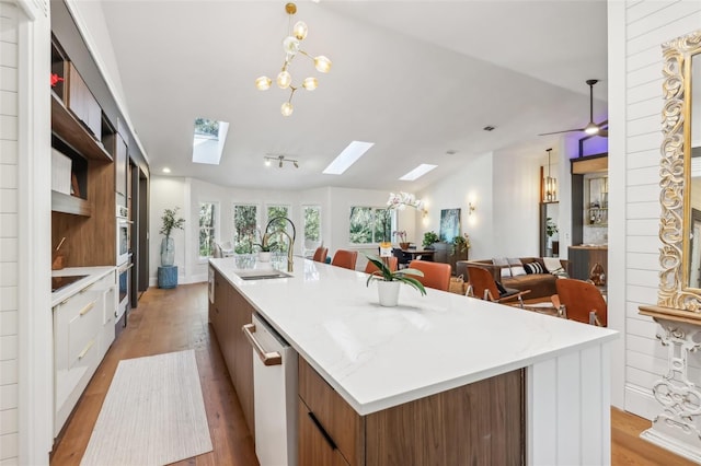 kitchen featuring light wood-type flooring, dishwashing machine, a kitchen island with sink, sink, and a chandelier