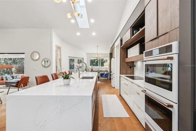 kitchen with a center island with sink, multiple ovens, sink, hanging light fixtures, and a notable chandelier