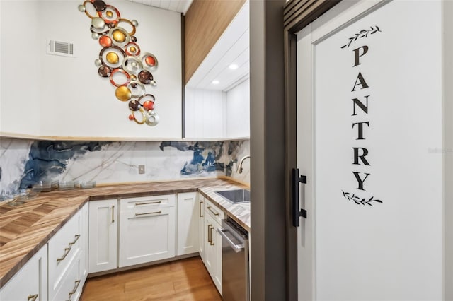 kitchen with wood counters, backsplash, sink, stainless steel dishwasher, and white cabinetry