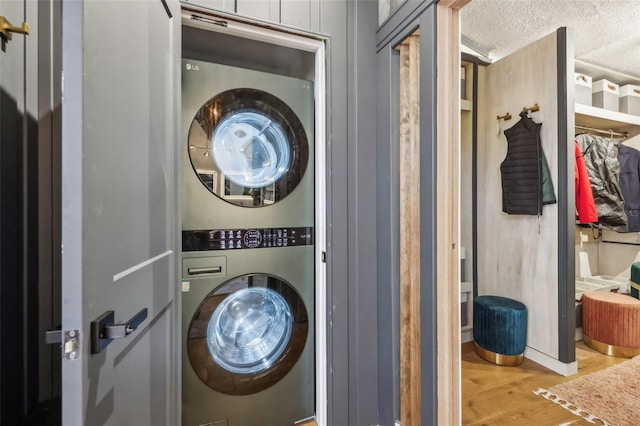 laundry room with a textured ceiling, stacked washer / drying machine, and light wood-type flooring