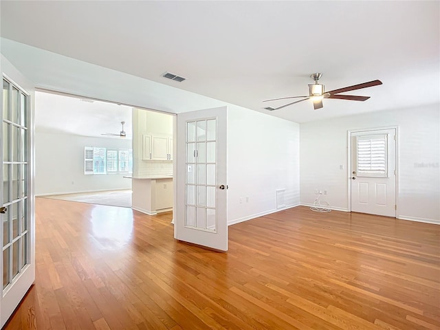 empty room with ceiling fan, light hardwood / wood-style floors, a wealth of natural light, and french doors