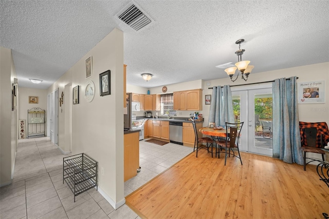 kitchen with light brown cabinetry, a textured ceiling, light tile patterned floors, a notable chandelier, and dishwasher